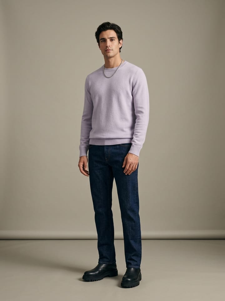 Man in a pale lavender knit sweater with straight dark denim jeans, heavy black leather boots and a silver chain necklace.