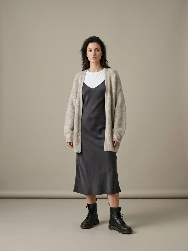 Woman wearing a charcoal satin slip dress over a plain white tee shirt, with an oversized oatmeal cardigan hanging open and black combat boots.