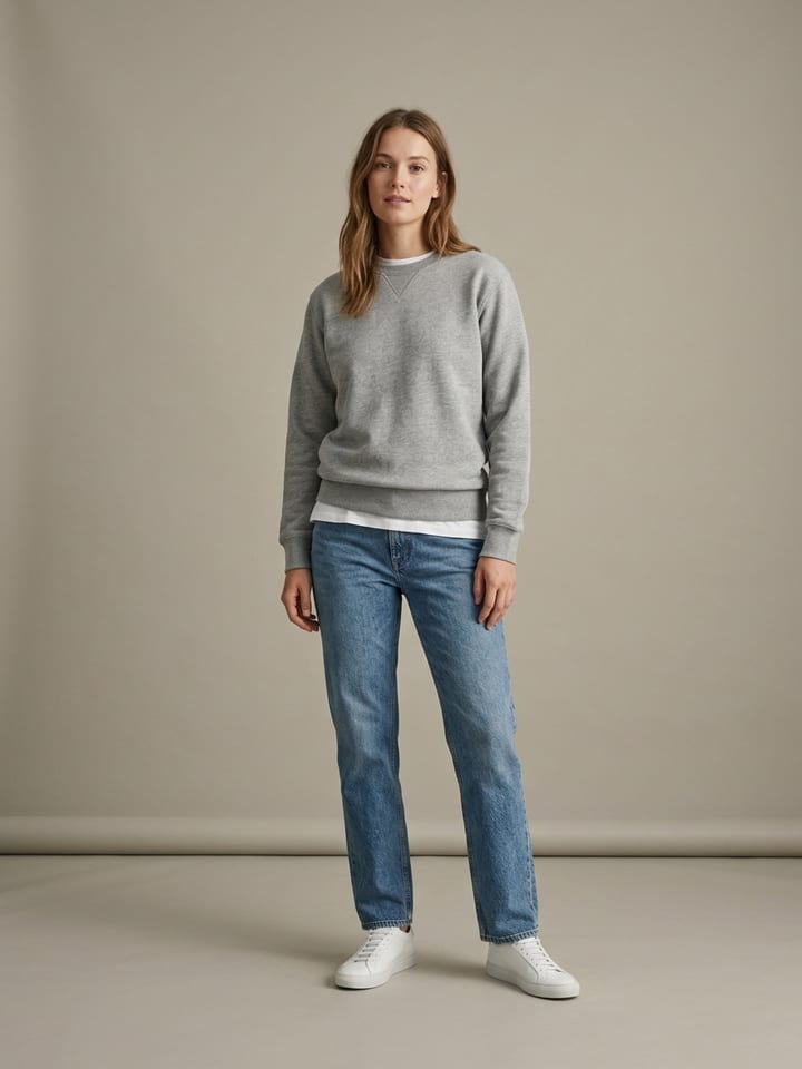 Woman in stonewash straight-leg jeans and a plain white tee under a grey crewneck sweatshirt, wearing plain white leather sneakers.