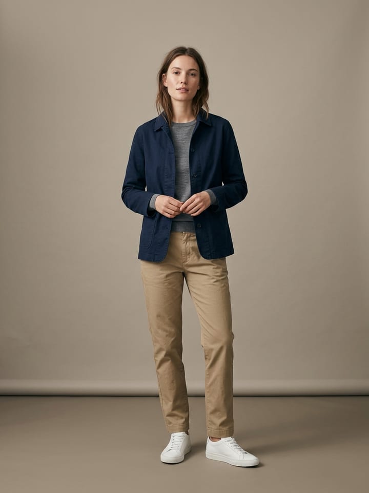 Woman in straight khaki chinos and a grey fine-knit long-sleeve top under an unstructured navy jacket, wearing plain white leather sneakers.